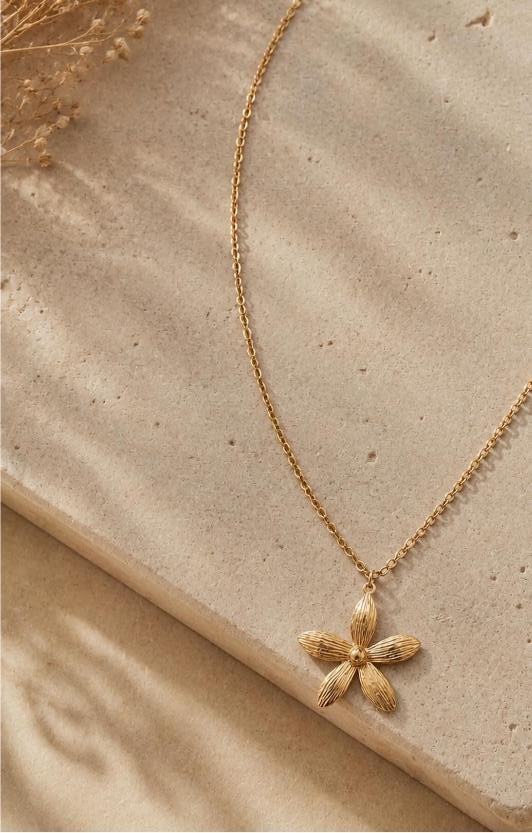 Fleur — fine gold chain with a single ribbed five-petal flower pendant on sand with palm shadow